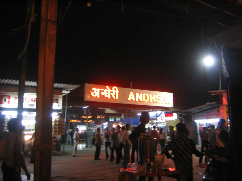 Andheri red light area, Mumbai — the station's glowing neon nameboard at night, hawker stalls and crowds below