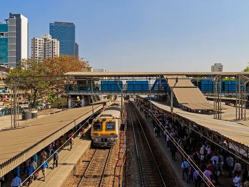 Dadar red light area, Mumbai — crowded platforms and a local train at Dadar station, towers rising behind