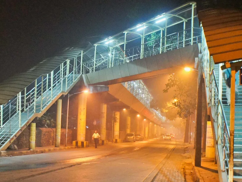 Ghatkopar red light area, Mumbai — the station footbridge over an amber-lit road in the night smog