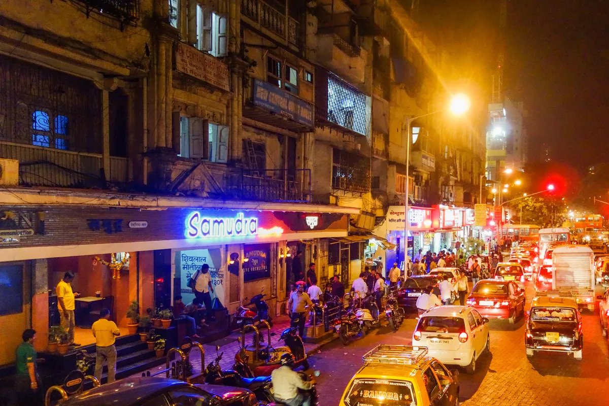 The Kamathipura belt at night — neon signs and taxi traffic outside old guest-house buildings near Dalal Estate, Mumbai Central